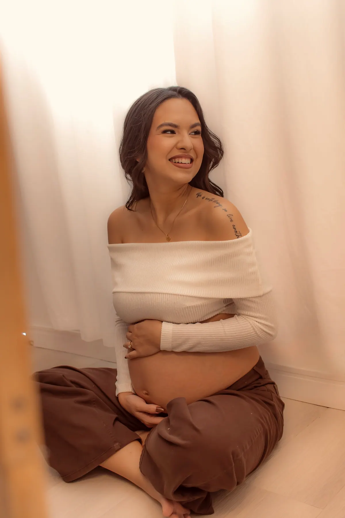 Gestante sorrindo sentada no chão, abraçando a barriga