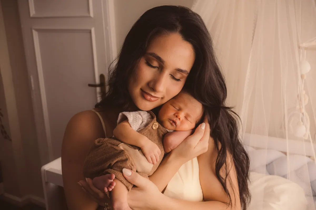 Mãe abraçando o bebê recém-nascido junto ao rosto, em luz suave